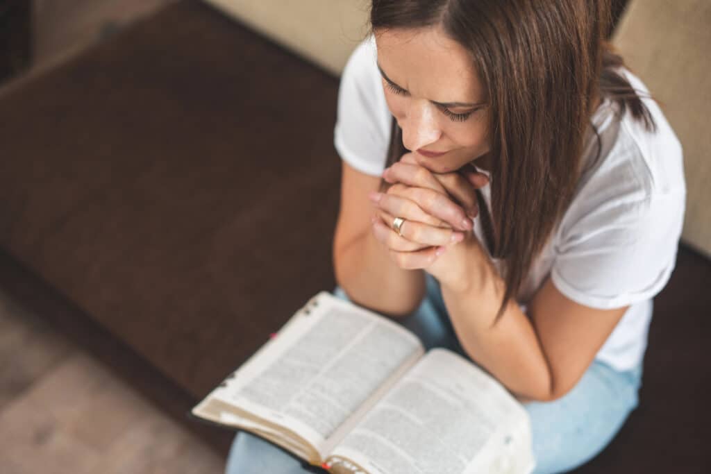 a woman sitting on a bench with her hands folded in prayer